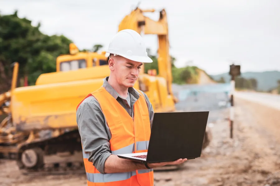 Practicum trainee in hi-vis checking a laptop on a job site